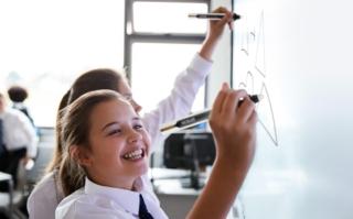 Female High School Students Wearing Uniform Using Interactive Whiteboard During Lesson Female High School Students Wearing Uniform Using Interactive Whiteboard During Lesson